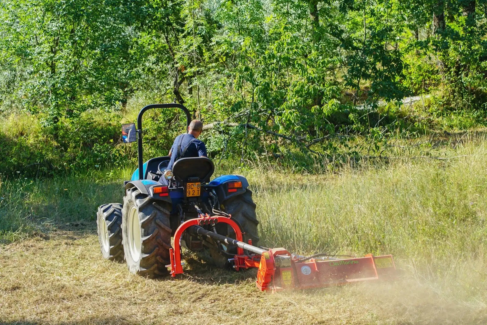 Blue tractor mowing tall grass.